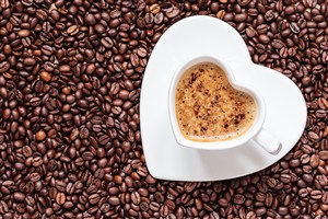 在咖啡豆上的心形咖啡杯高清摄影图