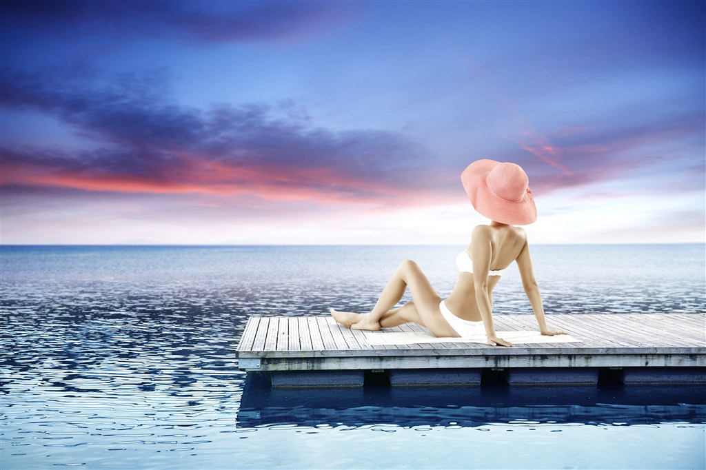 穿着三点式泳衣戴着遮阳帽坐在码头上的女性高清图片 