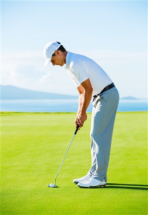 在草地上弯腰低头打高尔夫球的男士侧面高清图片