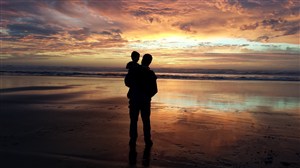 父亲抱着儿子海滩看日落背影