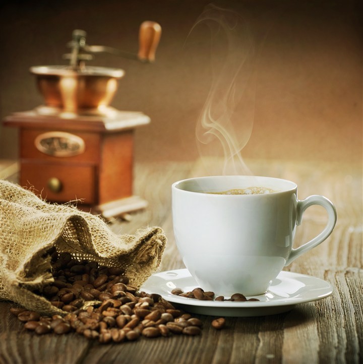 咖啡豆旁边冒着香气的白色咖啡高清摄影图片