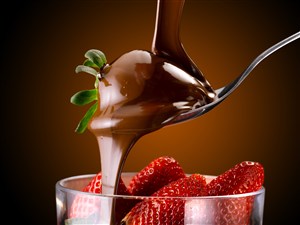 往杯子里的草莓倒巧克力酱的高清摄影图片