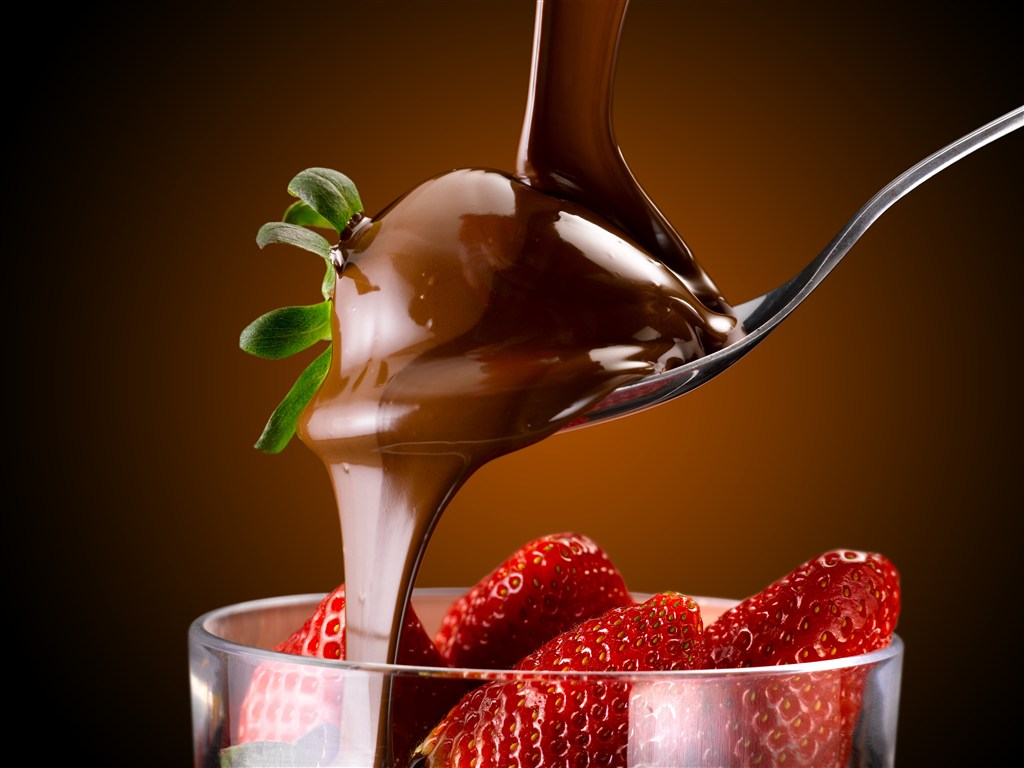 往杯子里的草莓倒巧克力酱的高清摄影图片